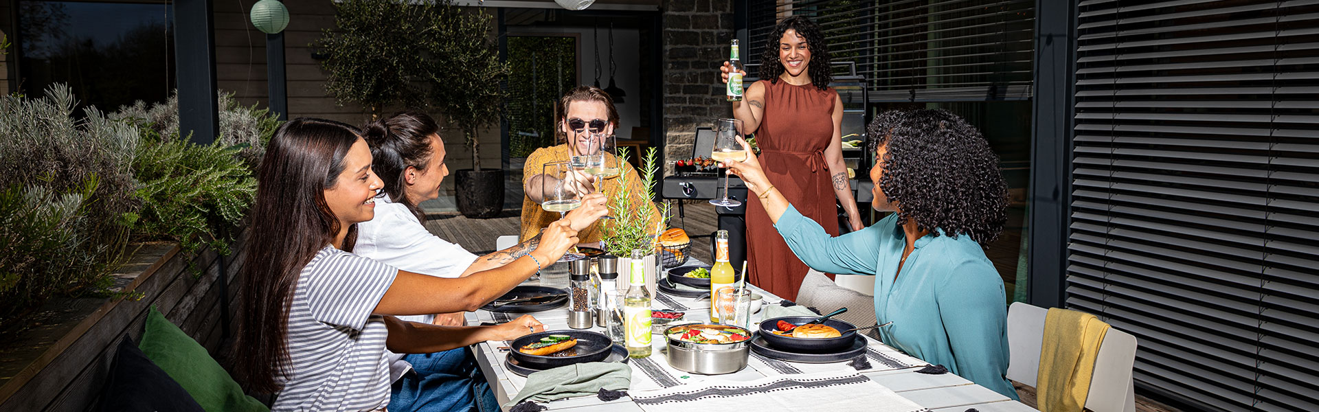 Freunde beim Grillen im Freien Grillabend mit Freunden im Freien, alle stoßen mit Gläsern an, Grill im Hintergrund.