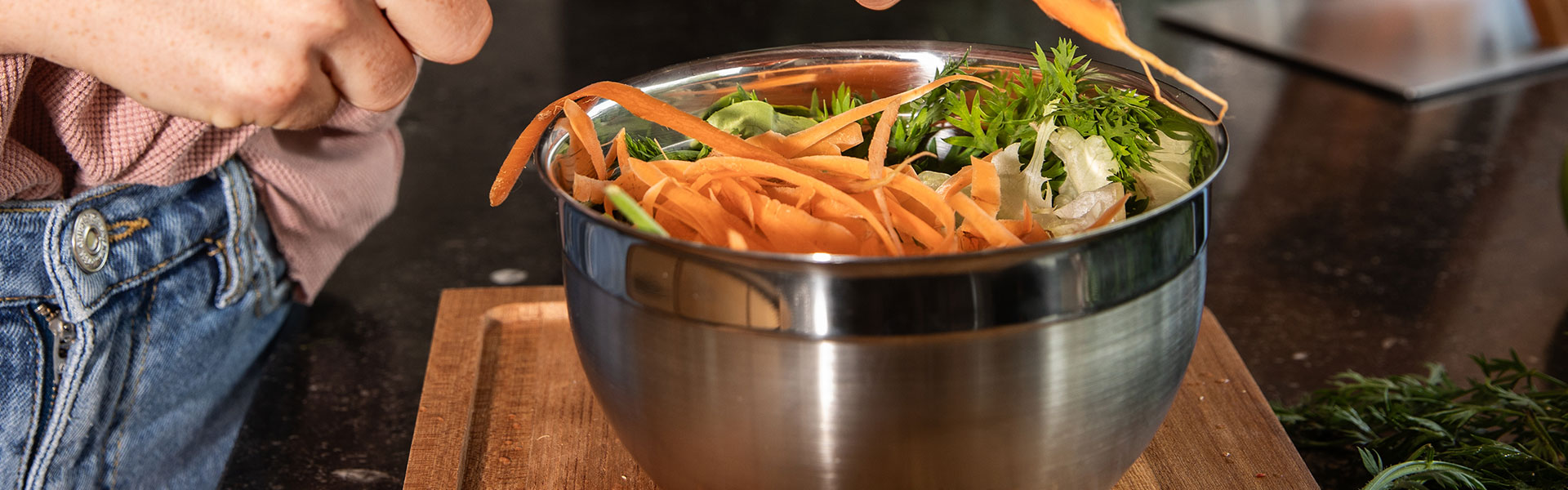 RÖSLE Edelstahl-Schüssel mit Gemüse Edelstahl-Schüssel mit frischem Gemüse, eine Person schält Karotten darüber.