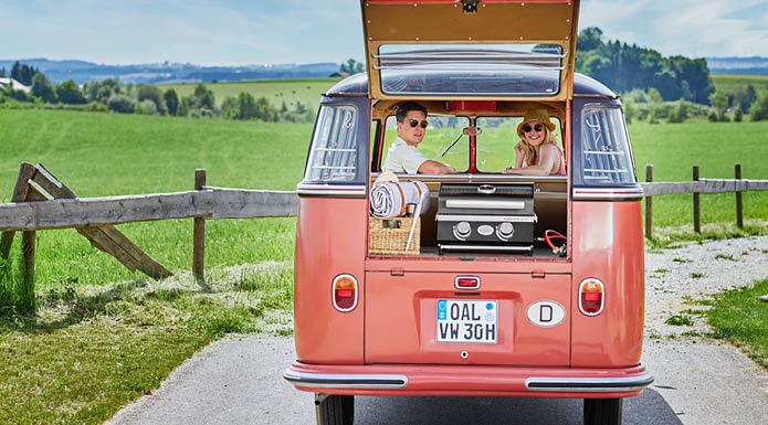 Couple sitting in VW Bully and looking back through open trunk