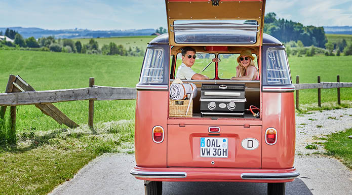 Gasgrill BBQ-Portable Videro G2-P Paar sitzt im VW Bully und schaut nach hinten durch offenen Kofferraum