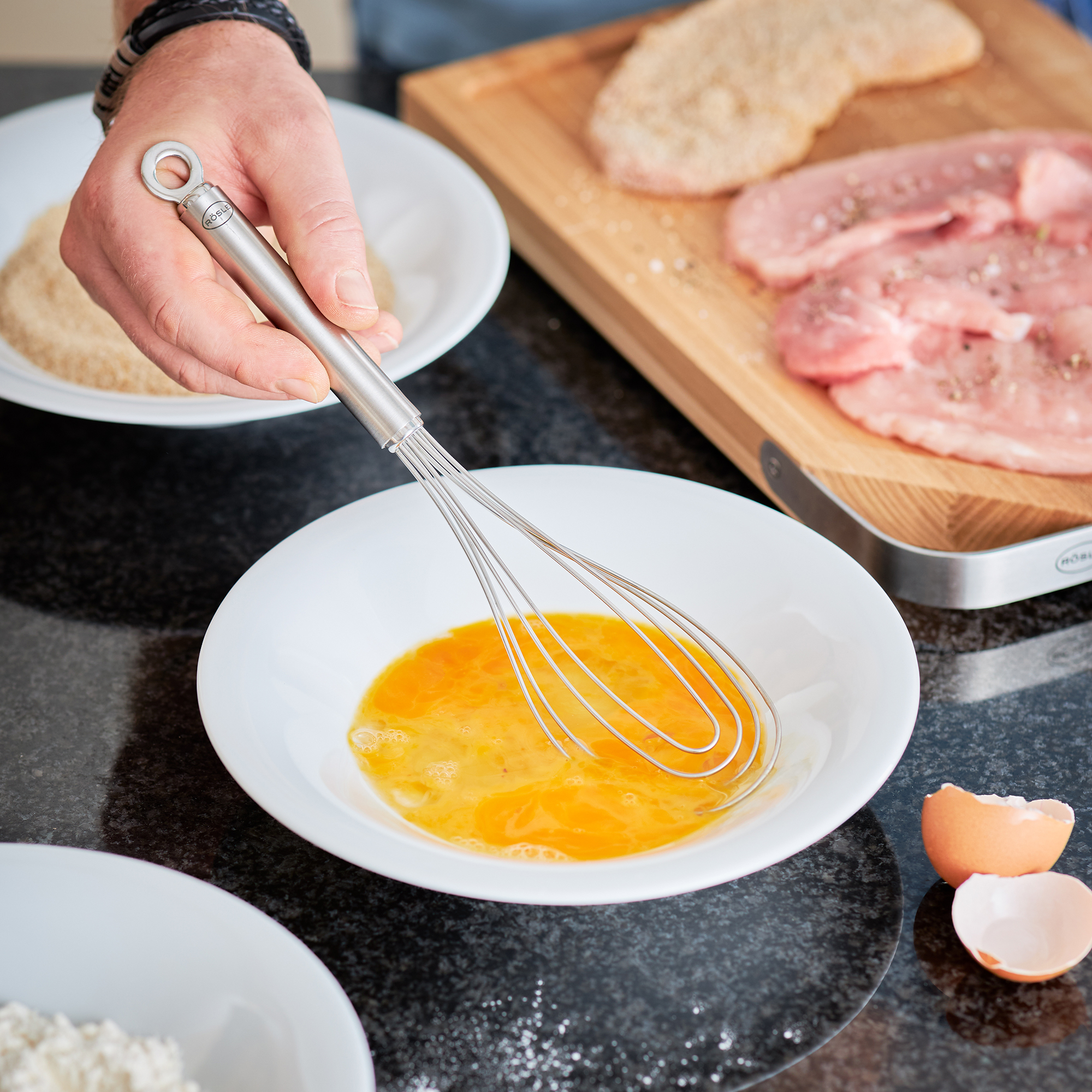RÖSLE stainless steel plate whisk 27 cm Stainless steel plate whisk, 27 cm, is used for whisking eggs in a white bowl.