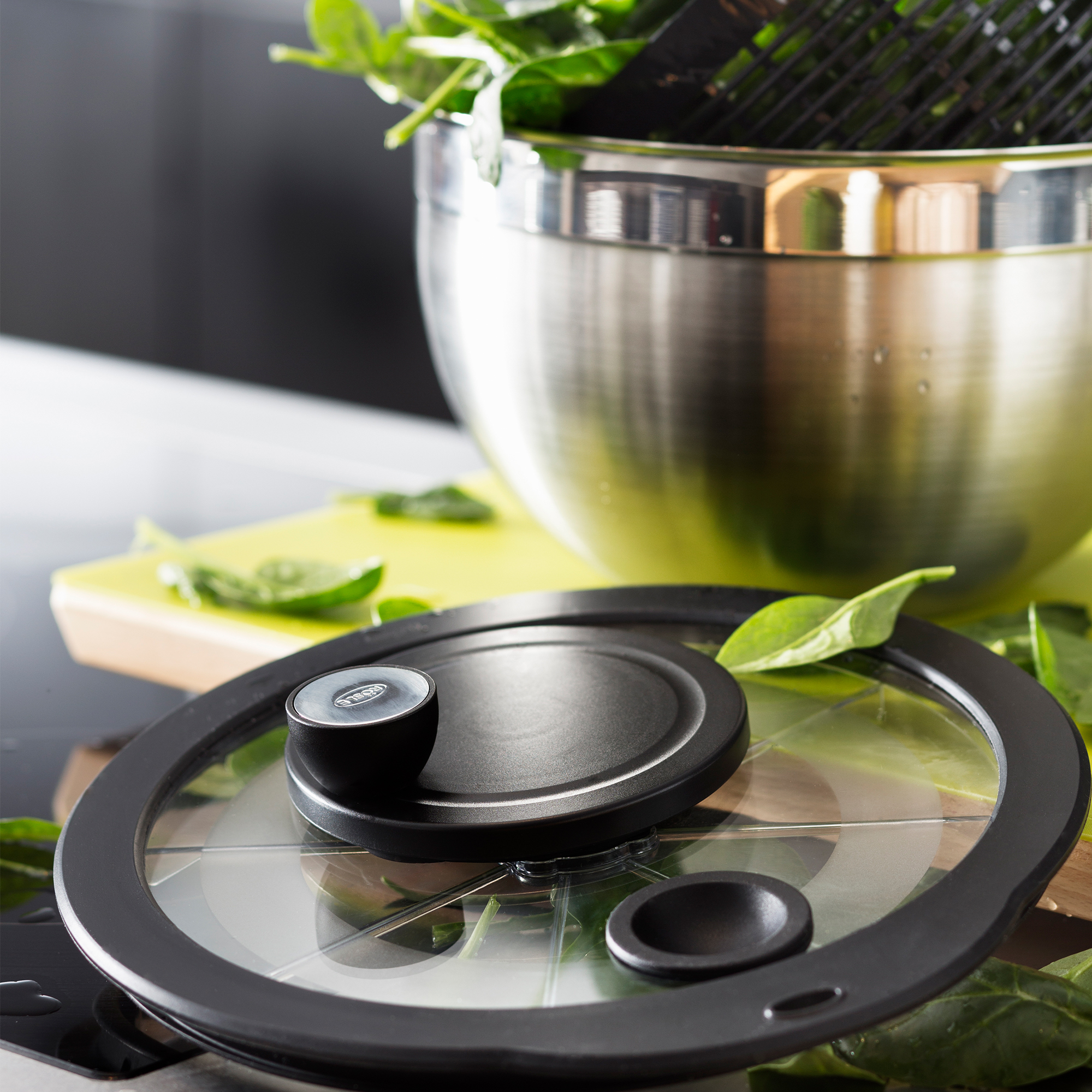 RÖSLE salad spinner Salad spinner with black lid and stainless steel bowl, filled with fresh spinach leaves.