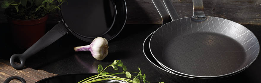 Eisenpfannen von RÖSLE Eisenpfannen in verschiedenen Formen und Größen, mit frischen Kräutern und Knoblauch.