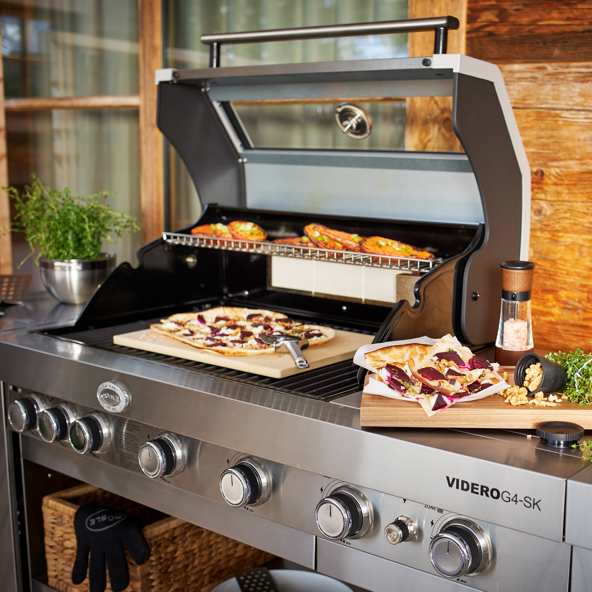RÖSLE VIDERO G4-SK Grill mit Pizzastein VIDERO G4-SK Grill mit geöffnetem Deckel, Pizzastein und belegten Pizzen auf dem Grillrost.