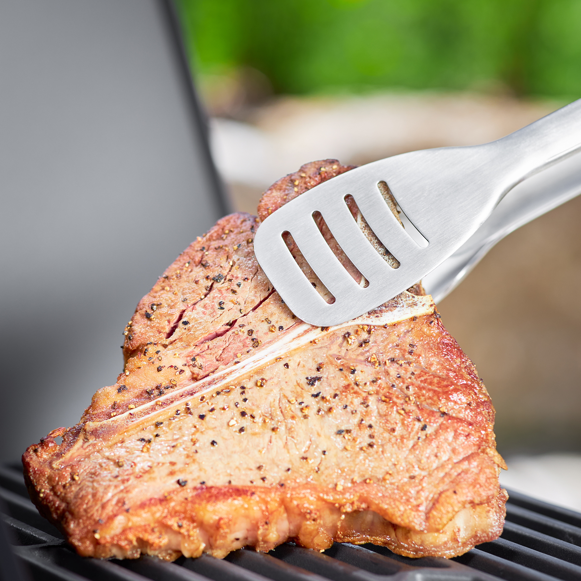 RÖSLE Premium Grillzange mit gegrilltem Fleisch Premium Grillzange aus Edelstahl hebt ein Stück gegrilltes Fleisch vom Grill.