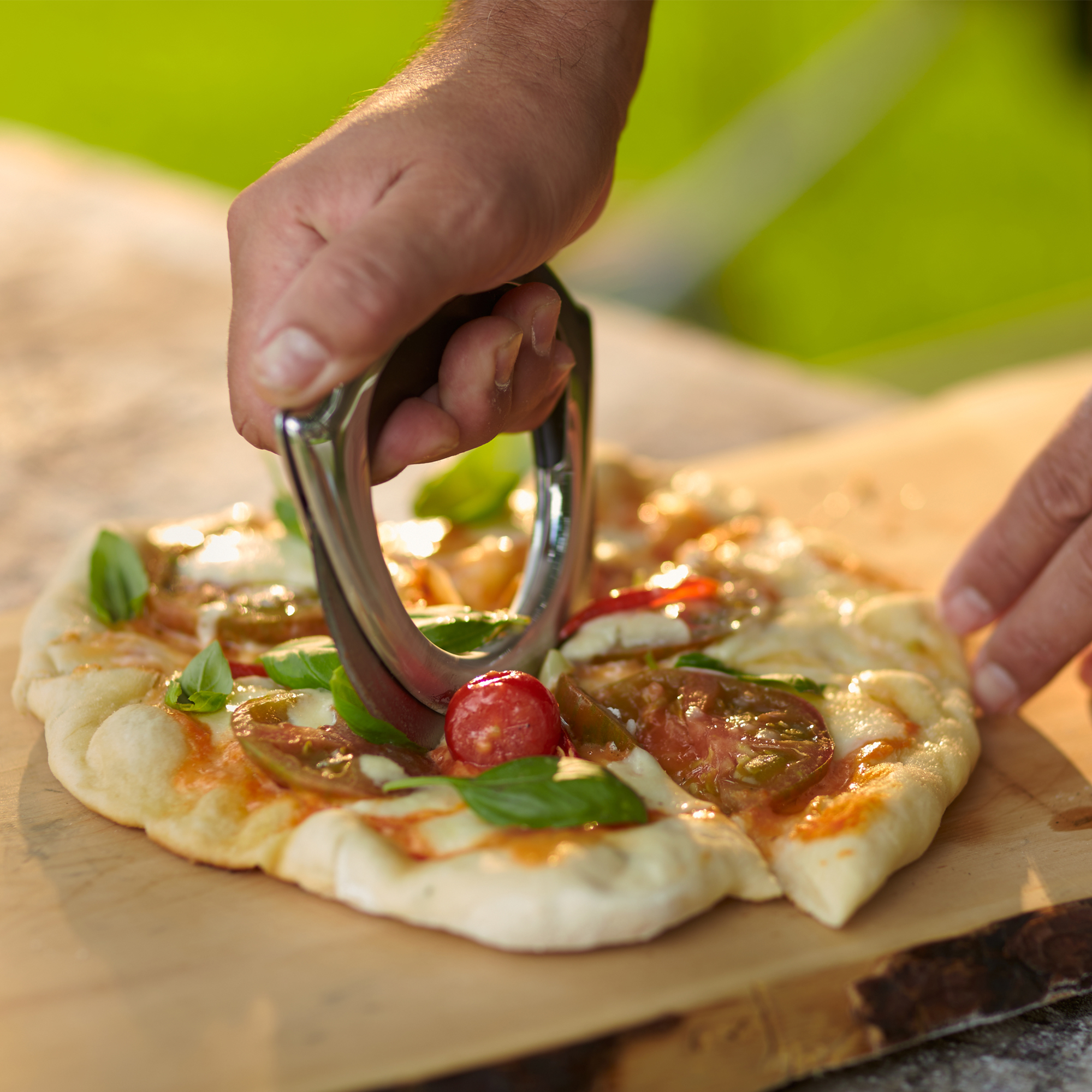 RÖSLE Pizzarad in Aktion Pizzarad aus Edelstahl, handgehalten, schneidet eine Pizza mit Tomatensauce und Artischocken.