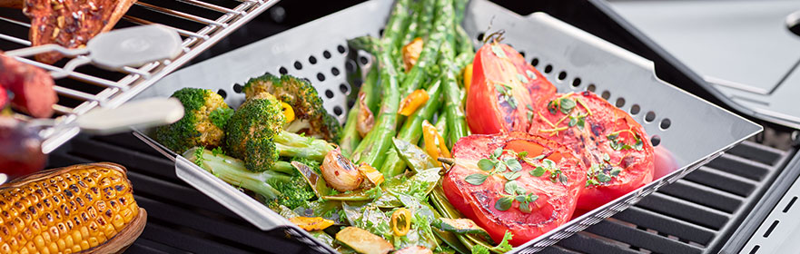 Grill accessoires met gegrilde groenten, zoals broccoli, asperges en tomaten, in een grillpan.