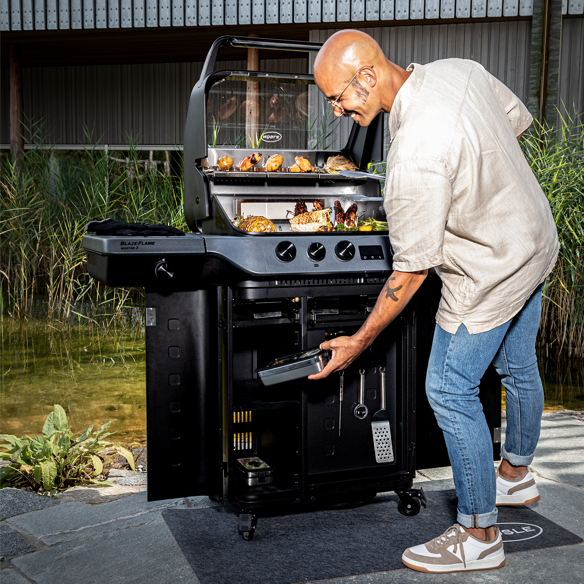 RÖSLE Blazeflame Master 3 Grill in Nutzung Blazeflame Master 3 Grill mit einem Mann, der eine Schublade öffnet, um Grillzubehör zu entnehmen.