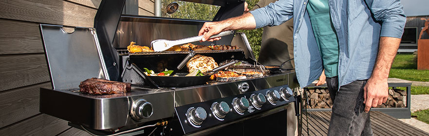Crickets Man stands at the grill with tongs and turns vegetables on the plancha plate