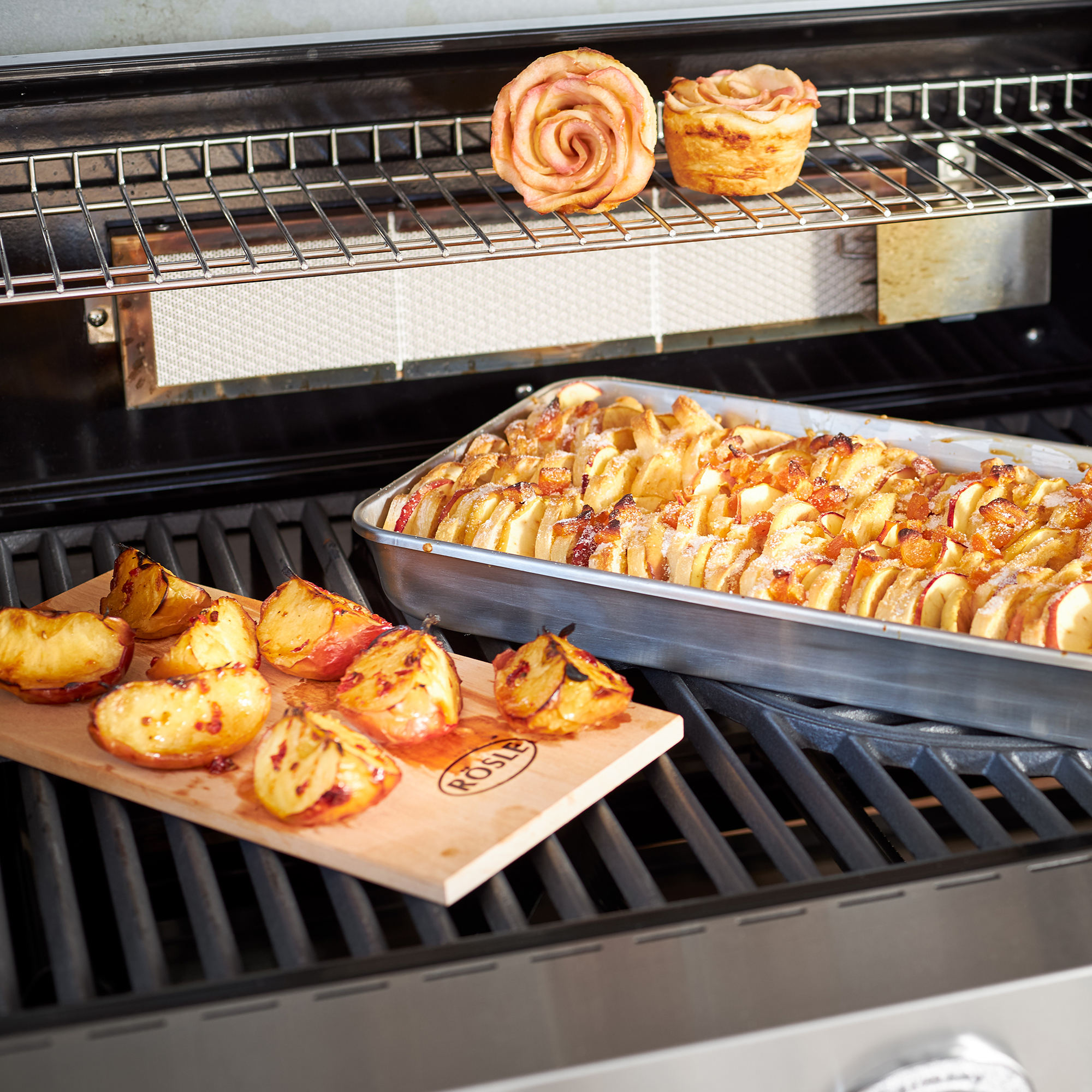 RÖSLE flavoured plank and baked fruit on the grill Flavoured alder plank with grilled apples and a tray of baked fruit on a grill.