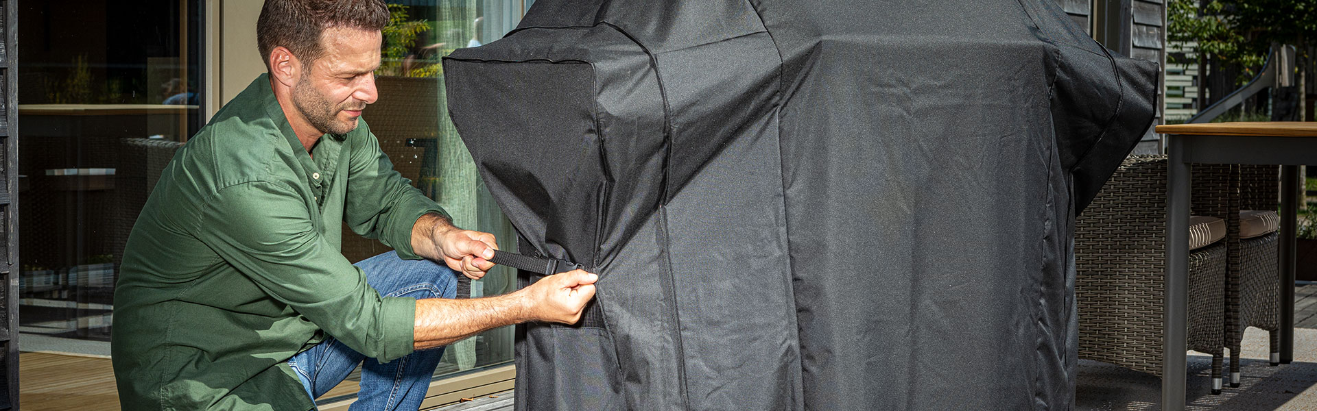 Mann mit Grillabdeckhaube Mann zieht eine schwarze Abdeckhaube für einen Grill an.