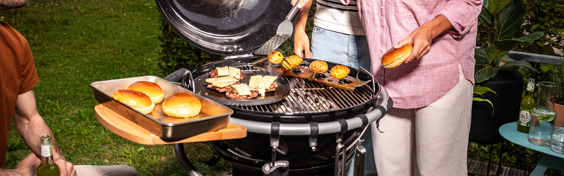 Holzkohlegrill mit Grillgut Holzkohlegrill mit Grillgut, darunter Burgerbrötchen und Fleisch, im Freien bei einer Grillparty.
