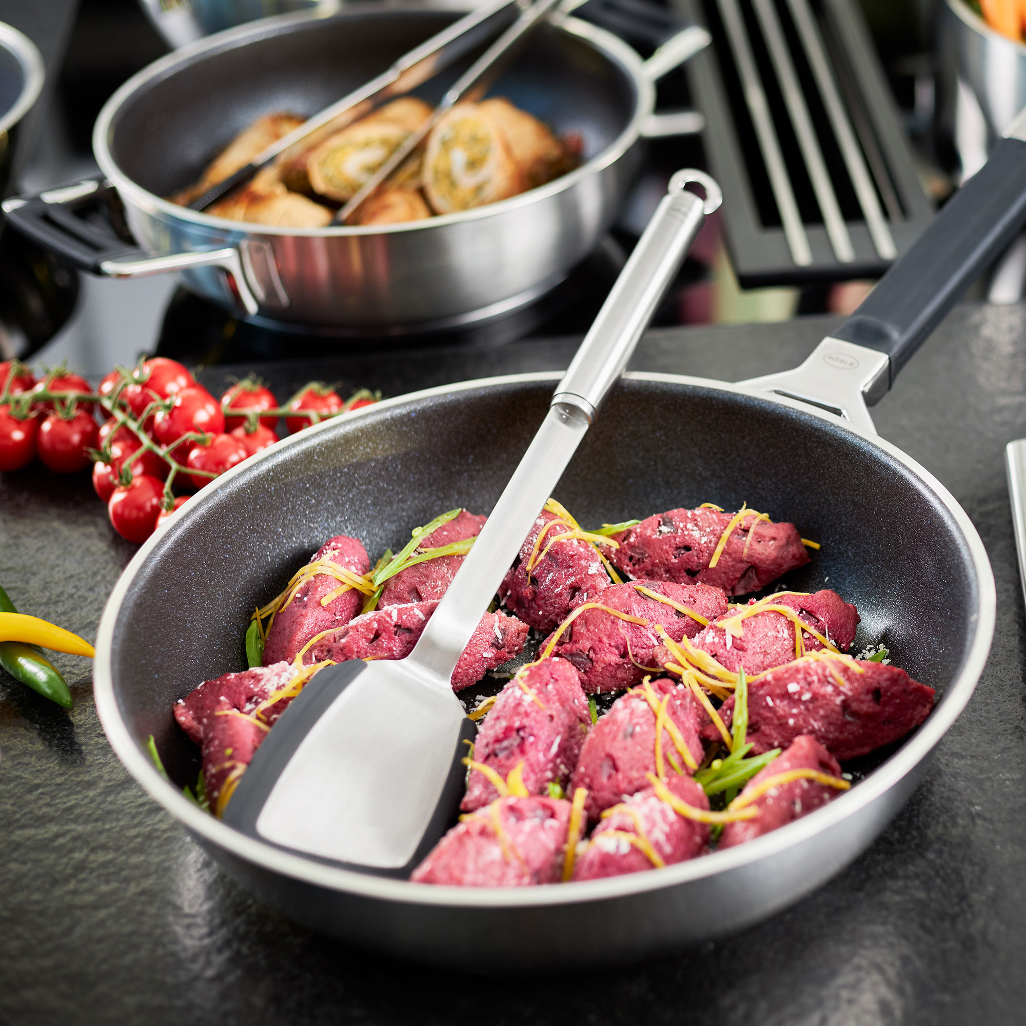 RÖSLE Küchenklassiker Set - Pfanne mit Fleisch und Kräutern Pfanne mit lila gefärbtem Fleisch und frischen Kräutern, auf einem modernen Kochfeld.