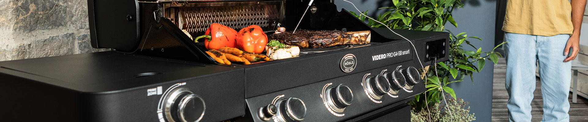 RÖSLE Gasgrill mit Grillgut Gasgrill mit Grillgut wie Gemüse und Fleisch auf dem Rost, schwarze Oberfläche, moderne Ausstattung.