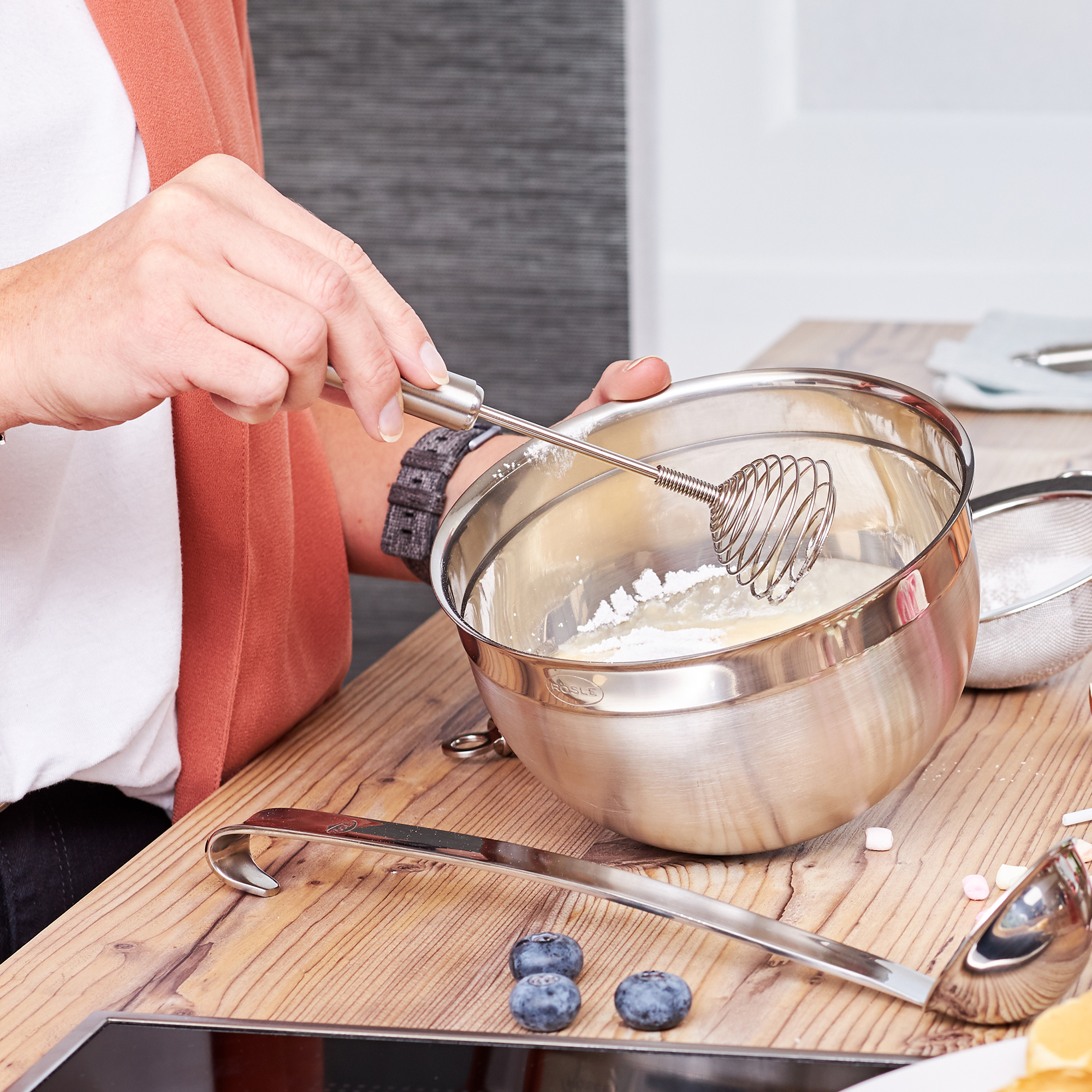 RÖSLE Rührschüssel mit Schneebesen Rührschüssel aus Edelstahl, hoch, 20 cm, mit Hand, die einen Schneebesen hält, auf einer Holzoberfläche.