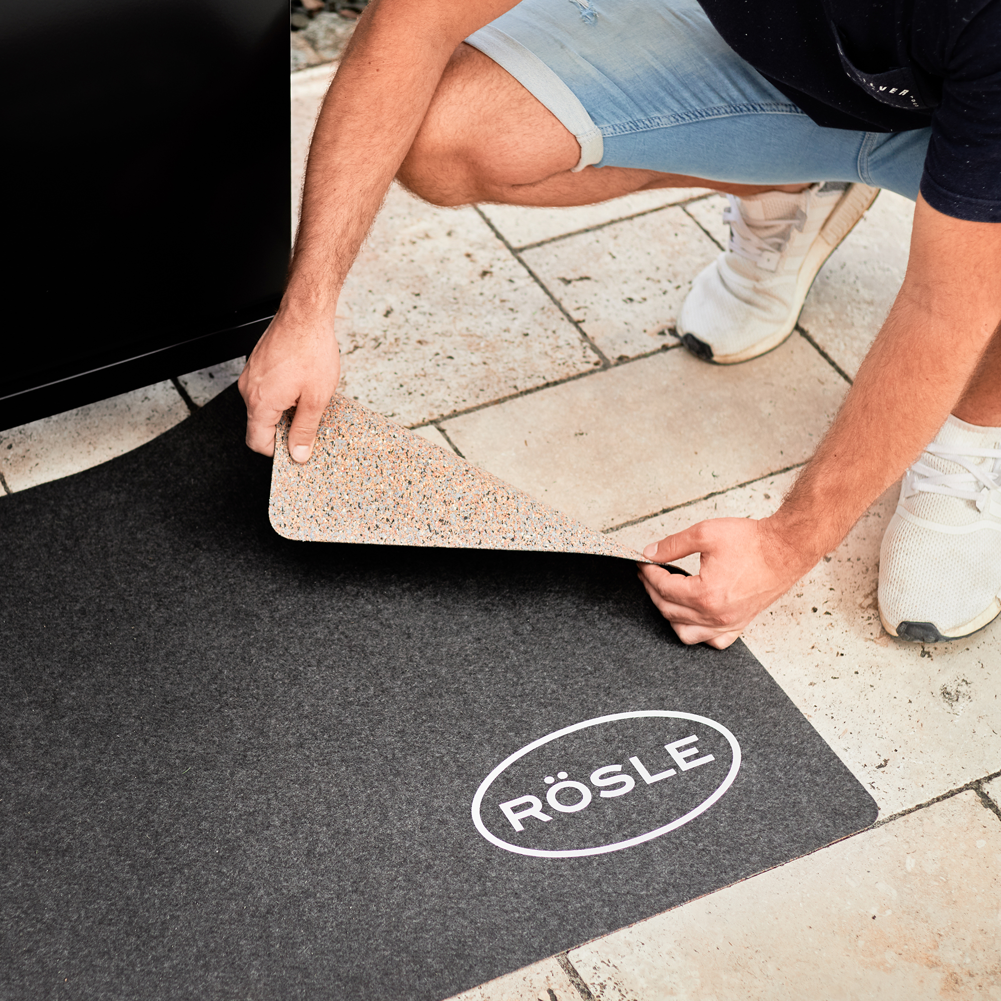 RÖSLE BBQ Grillunterlage BBQ Grillunterlage in schwarz, wird von einer Person auf dem Boden ausgelegt.