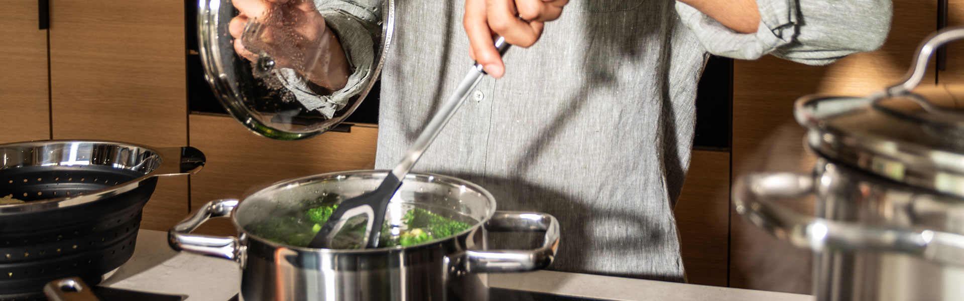 RÖSLE Kochtopf mit Gemüse Kochtopf aus Edelstahl mit Gemüse, Person mit grauem Hemd rührt mit einem Kochlöffel.