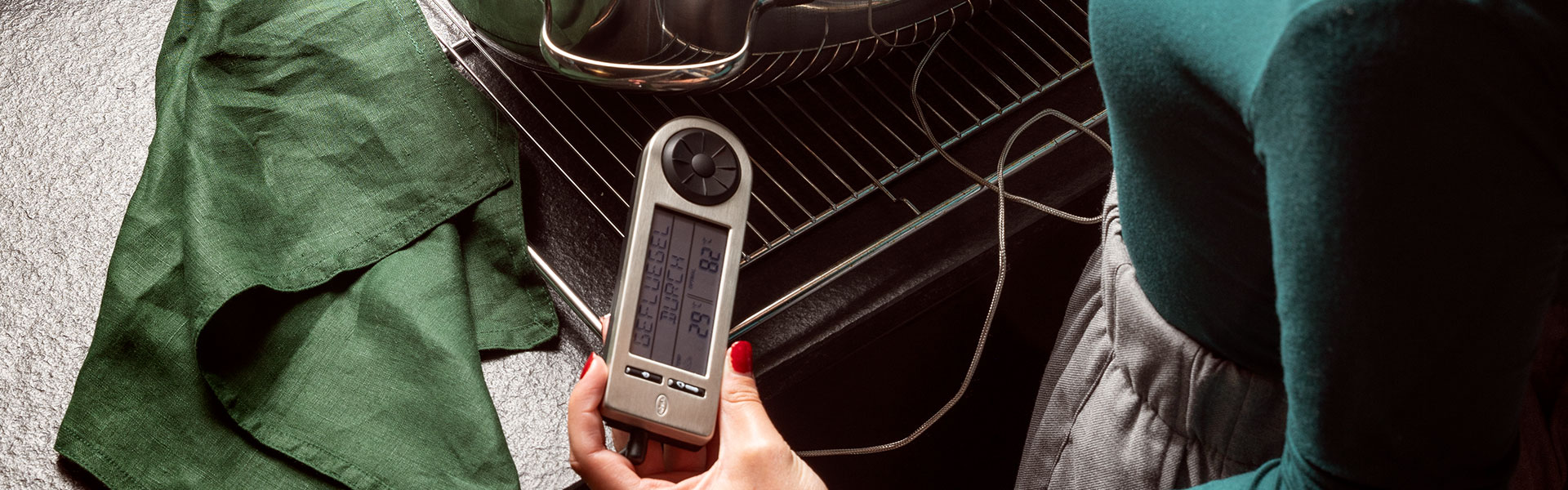 RÖSLE Küchenthermometer Küchenthermometer in Hand, mit digitalem Display und Temperaturmesskabel, auf einem Grillrost.