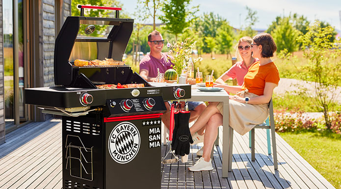 Friends are sitting at the table and in front of them is the FC Bayern gas barbecue with barbecue food
