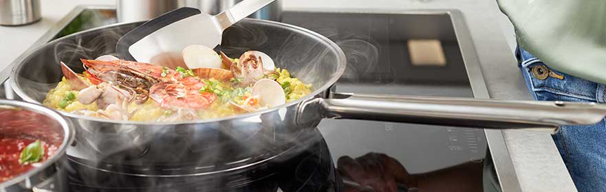 RÖSLE Elegance Pfanne mit Meeresfrüchten Elegance Pfanne mit Meeresfrüchten und Gemüse auf einem Induktionskochfeld, dampfend.