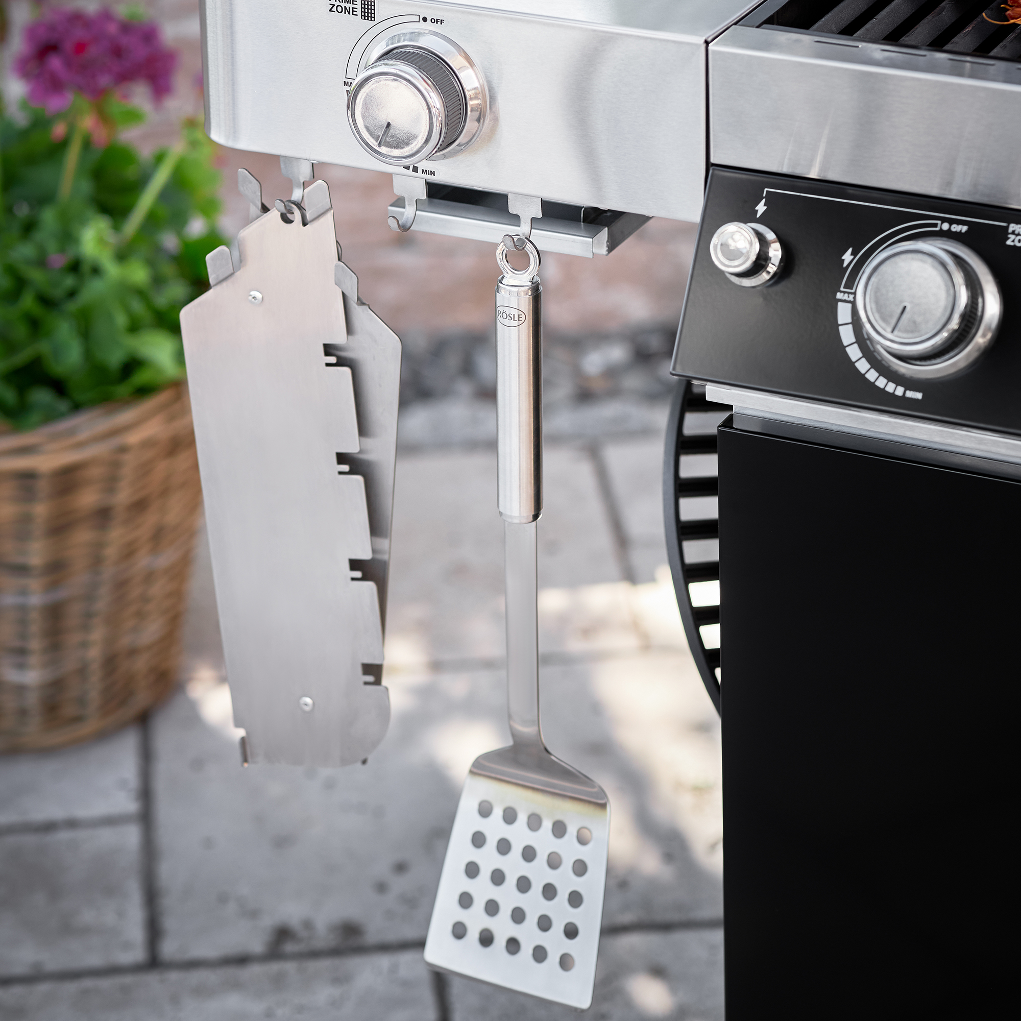 Grillwender aus Edelstahl, mit perforierter Kelle, hängt an einem Grill.