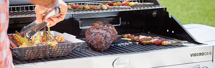 Gasgrill VIDERO G6 von RÖSLE mit Grillgut Gasgrill VIDERO G6 mit Grillgut, darunter Gemüse und ein Braten in einer Grillpfanne.