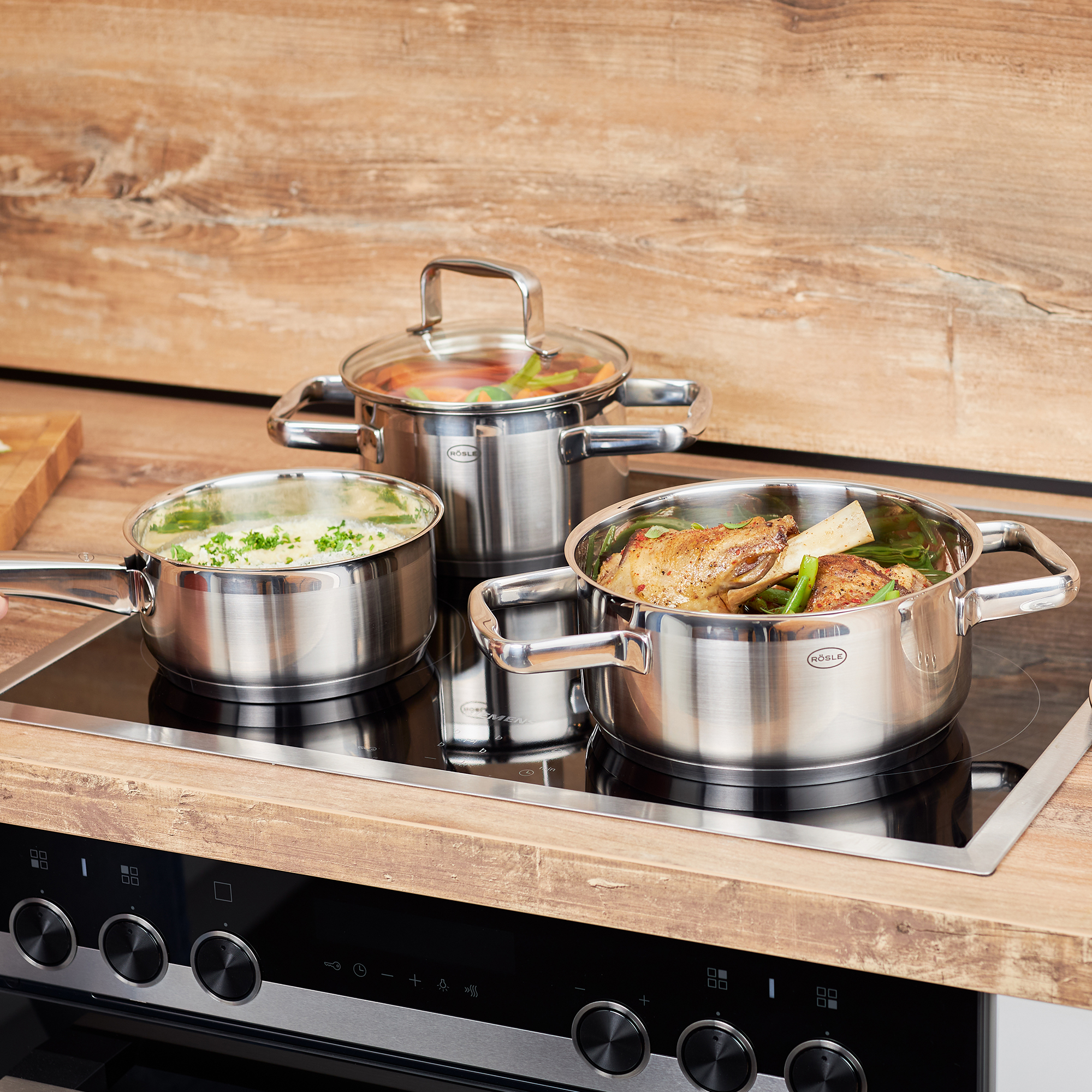 RÖSLE Stielkasserolle auf Herd Stielkasserolle 16 cm aus Edelstahl, auf einem Herd mit zwei weiteren Töpfen, die verschiedene...