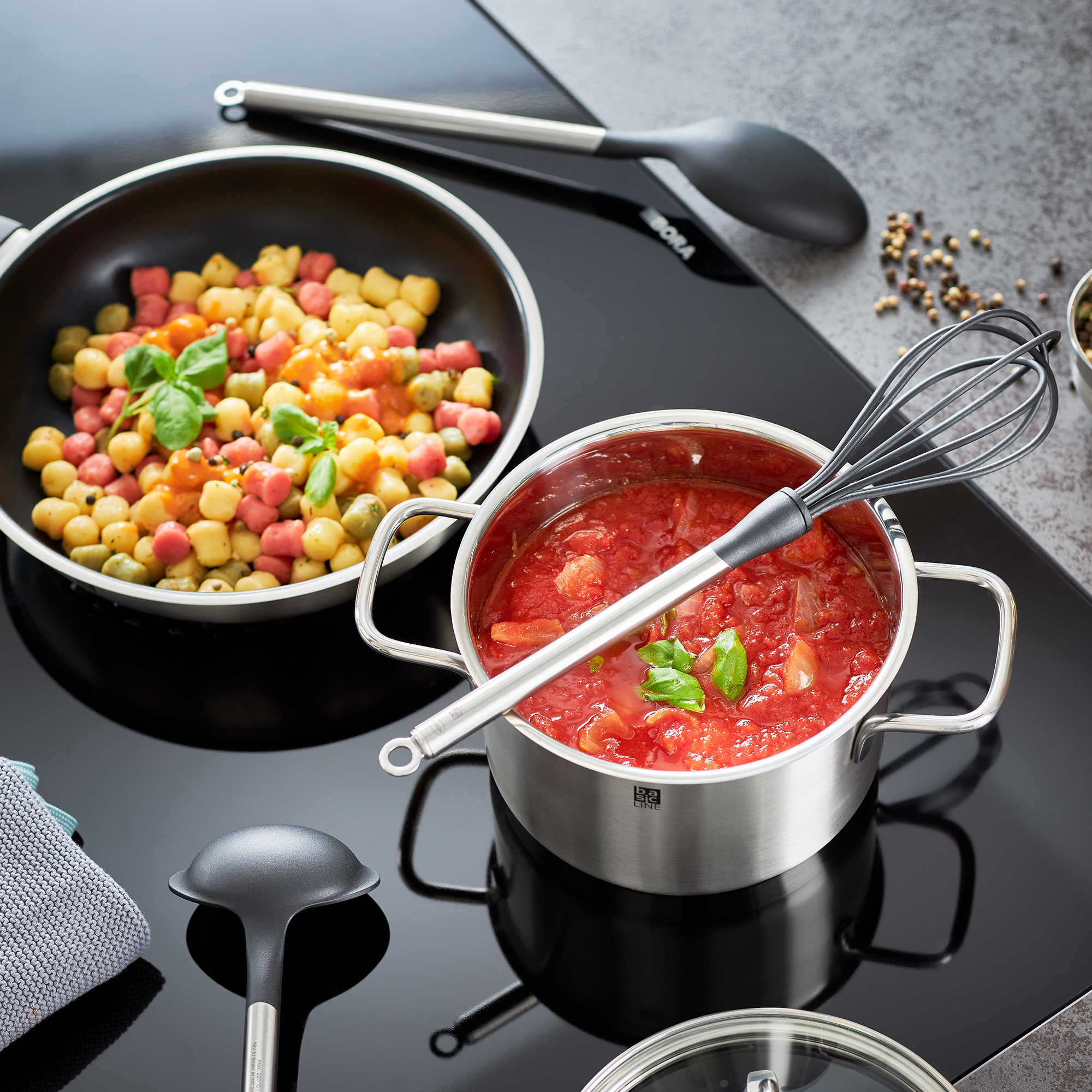 RÖSLE Schneebesen und Kochgeschirr auf der Arbeitsfläche Schneebesen aus Edelstahl, 31 cm, neben einem Topf mit Tomatensoße und einer Pfanne mit buntem...
