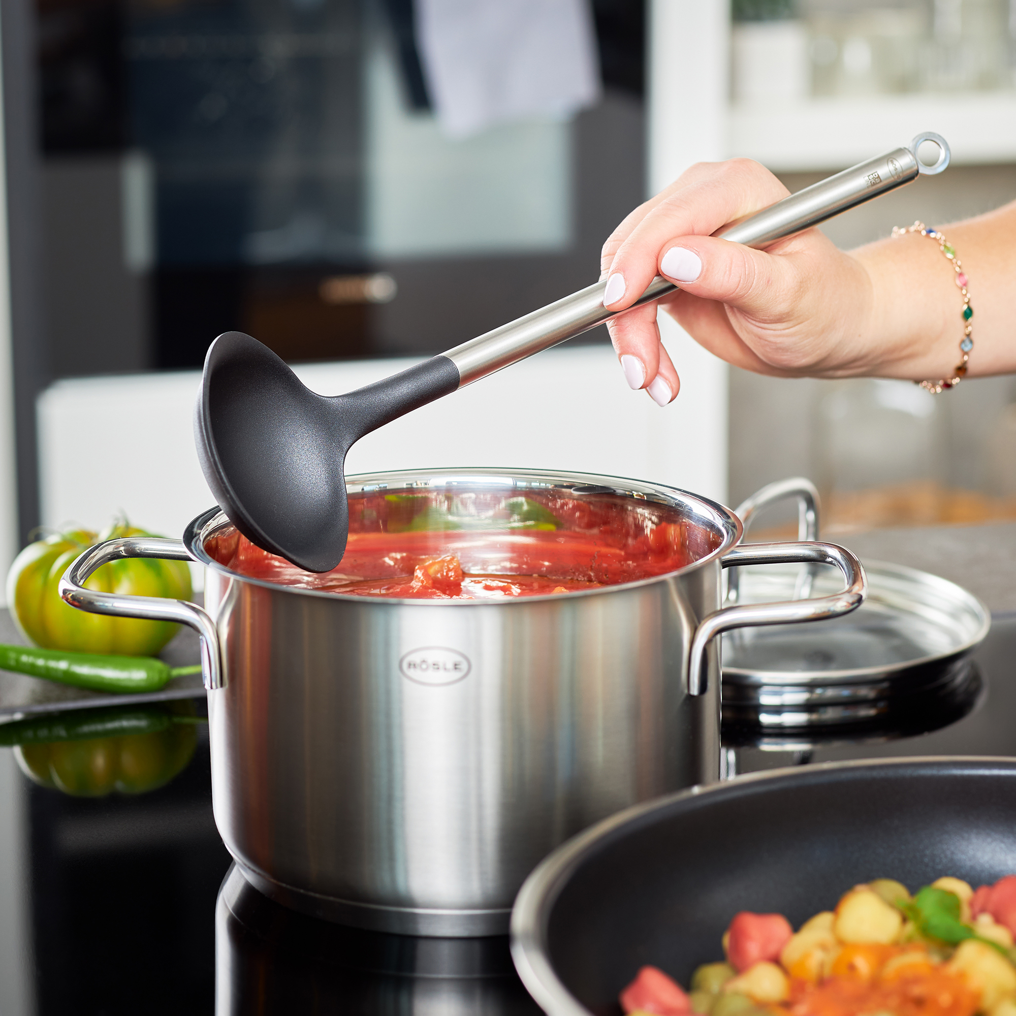 RÖSLE Sossenlöffel 28 cm Sossenlöffel aus schwarzem Kunststoff, in einem Topf mit Tomatensauce, Hand greift nach dem...