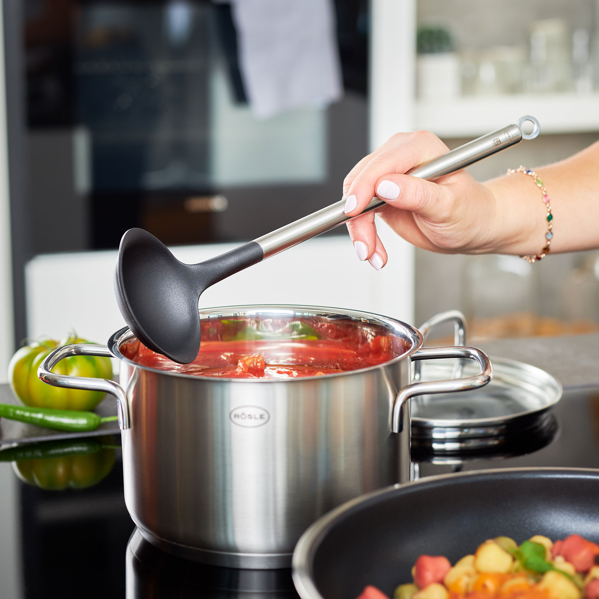 RÖSLE Gourmet-Set mit Schöpflöffel und Topf Gourmet-Set mit einer Hand, die einen schwarzen Schöpflöffel aus Kunststoff in einen Edelstahl-Topf...