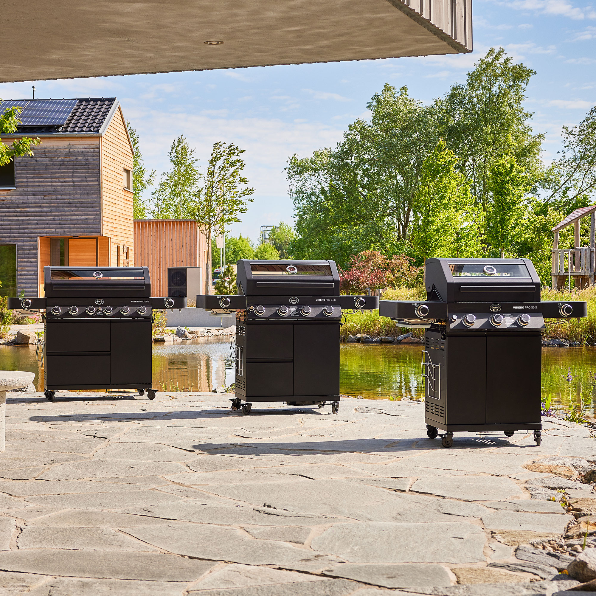 RÖSLE Gasgrill Videro G4-S PRO Gasgrill Videro G4-S PRO, drei Modelle auf einem Steinweg vor einem Teich und Bäumen.