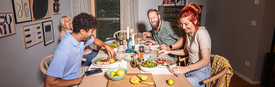 Essen Vier Freunde sitzen zusammen am Tisch und lachen beim Essen