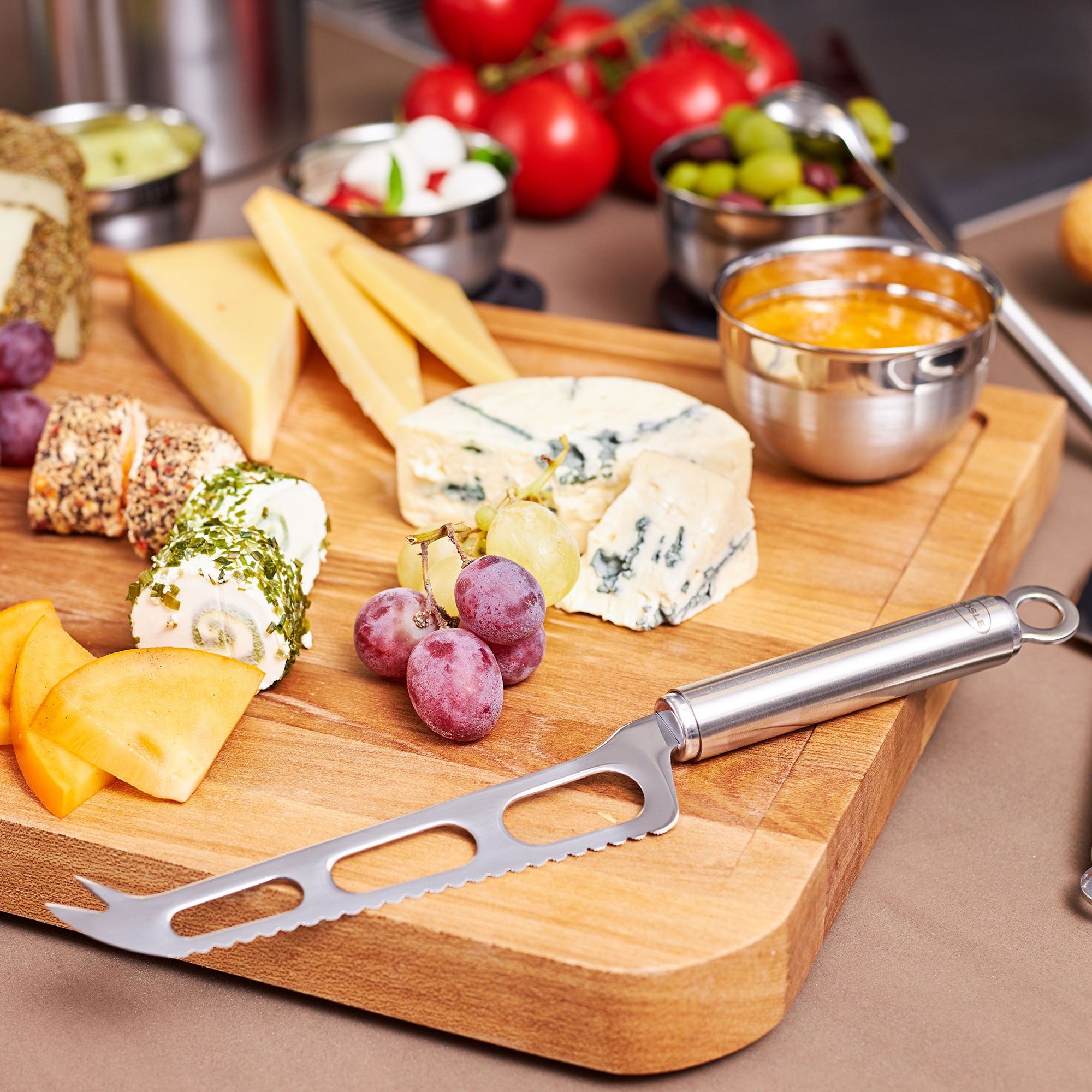 RÖSLE Käse-Set auf Holzbrett Käse-Set mit Käsemesser auf einem Holzbrett, umgeben von verschiedenen Käsesorten und Trauben.