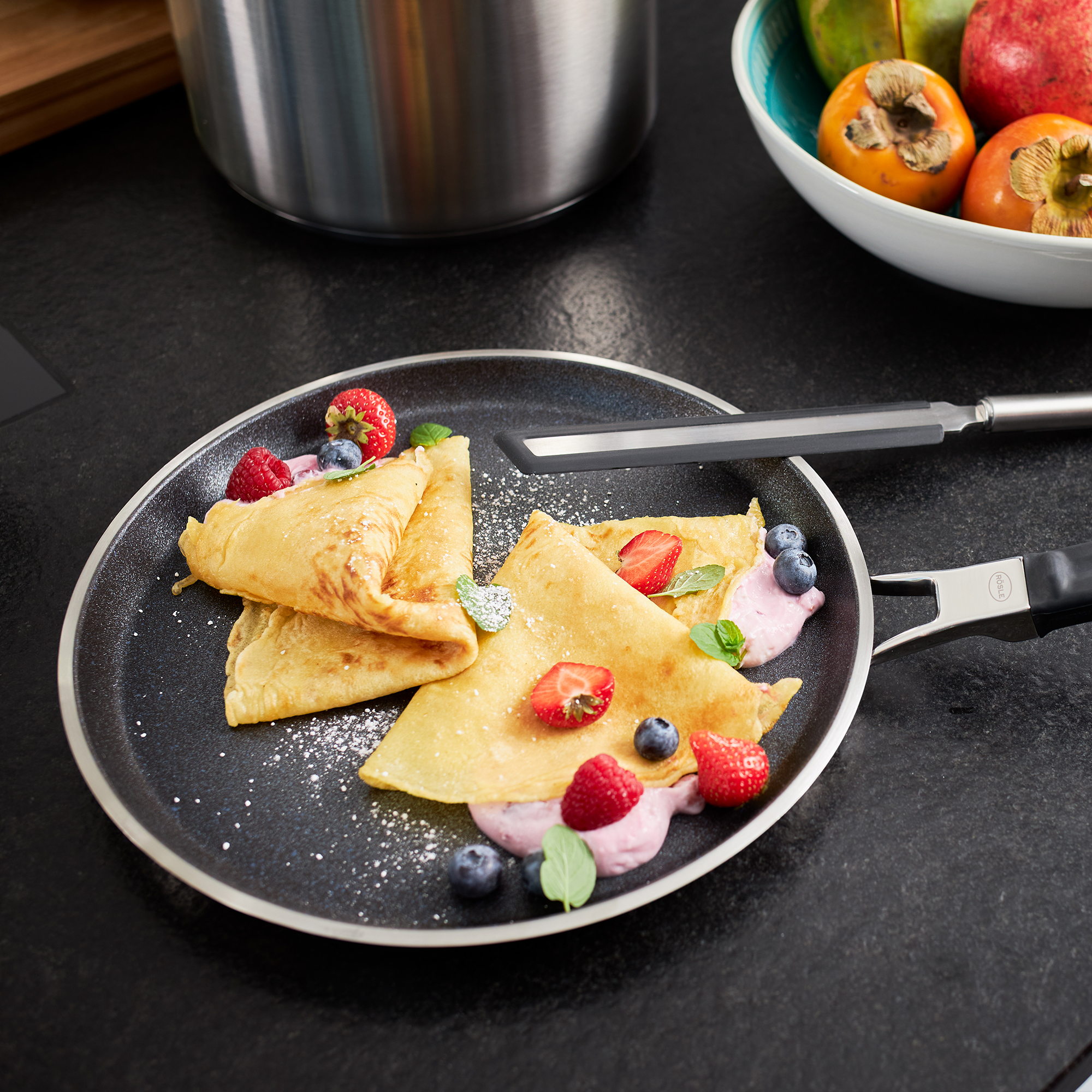 RÖSLE crepes pan with crepes and fruit Crepes pan, 28 cm, with filled crepes, fresh berries and a bowl of fruit in the background.