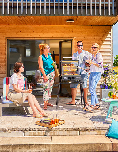 Friends stand around electric grill and laugh together