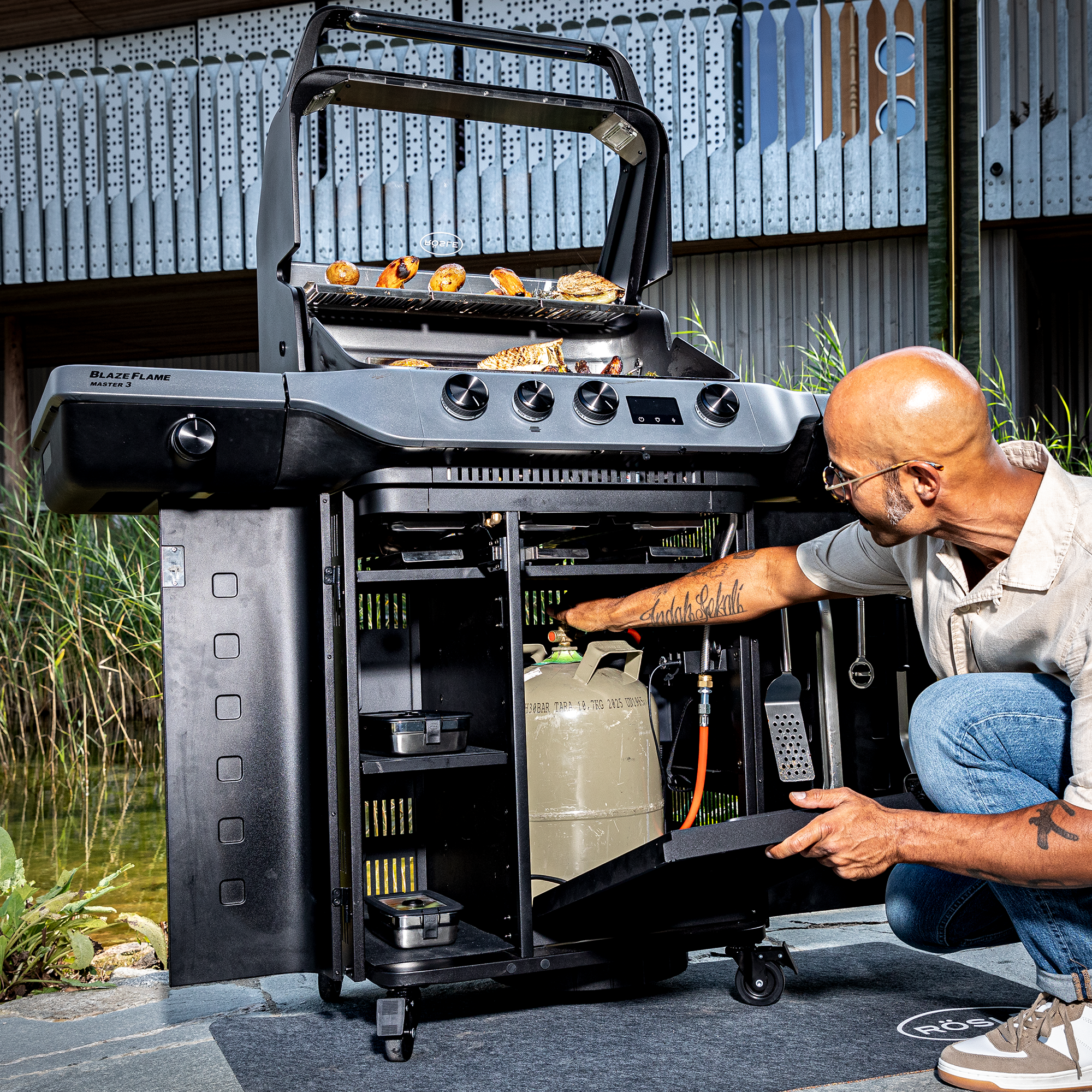 Blazeflame Master Grill mit geöffnetem Unterschrank, Benutzer überprüft die Gasflasche.