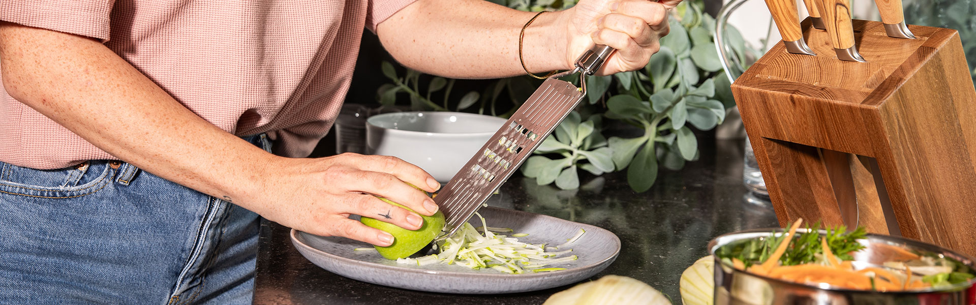 RÖSLE Reibe mit grünem Apfel Reibe in Verwendung, eine Person reibt einen grünen Apfel auf einem Teller.
