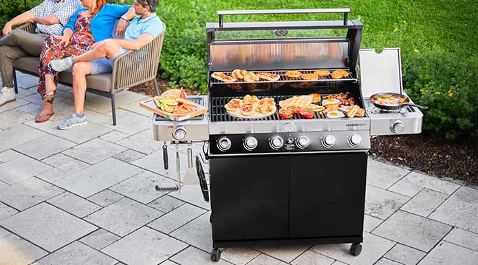Gas grill with open lid and various grilled food on grill grate.