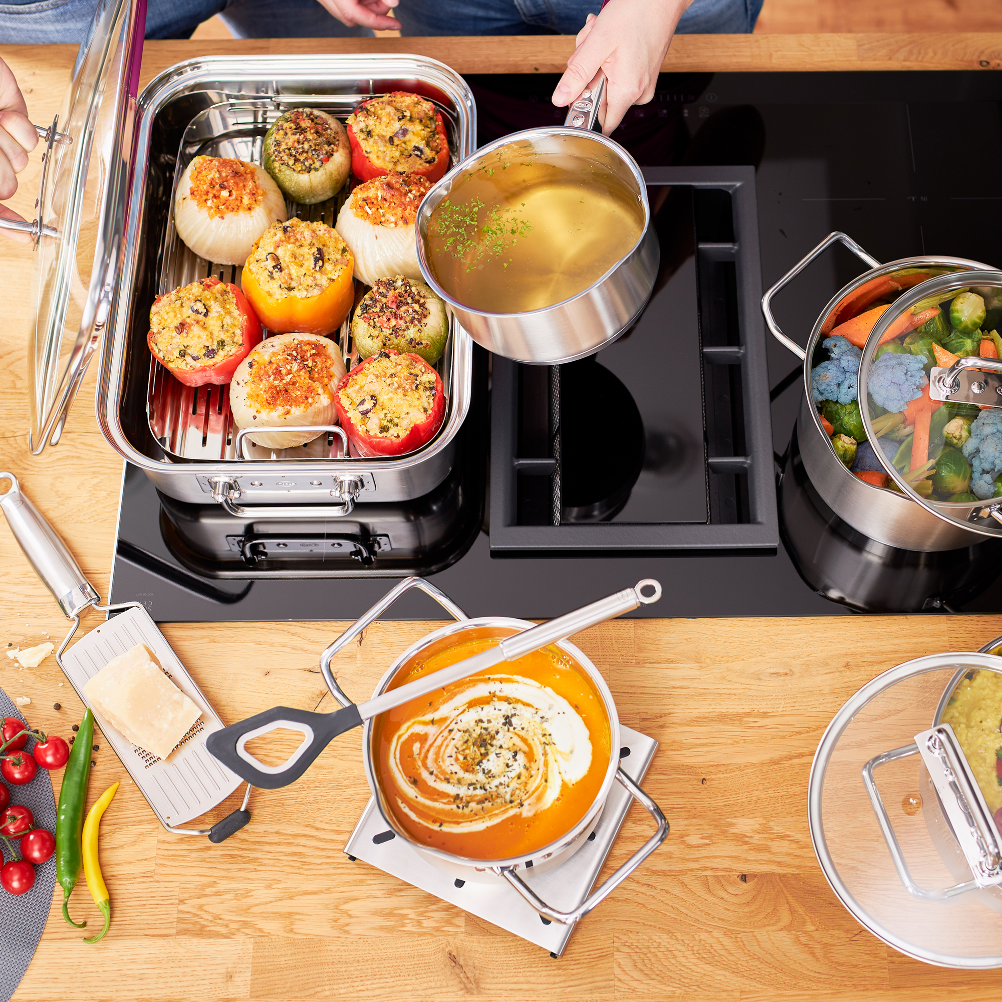 RÖSLE Kochtopf mit gefüllten Paprika und Gemüse Kochtopf mit gefüllten Paprika und Gemüse auf einem Herd, eine Person gießt Brühe ein.