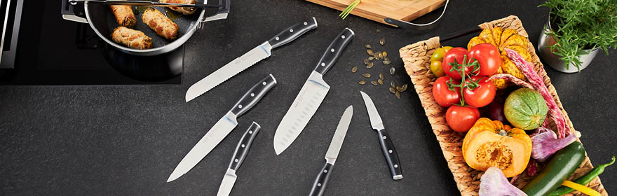 Knives + Cutters Kitchen knife set with different types of knives on a work surface, surrounded by fresh vegetables...