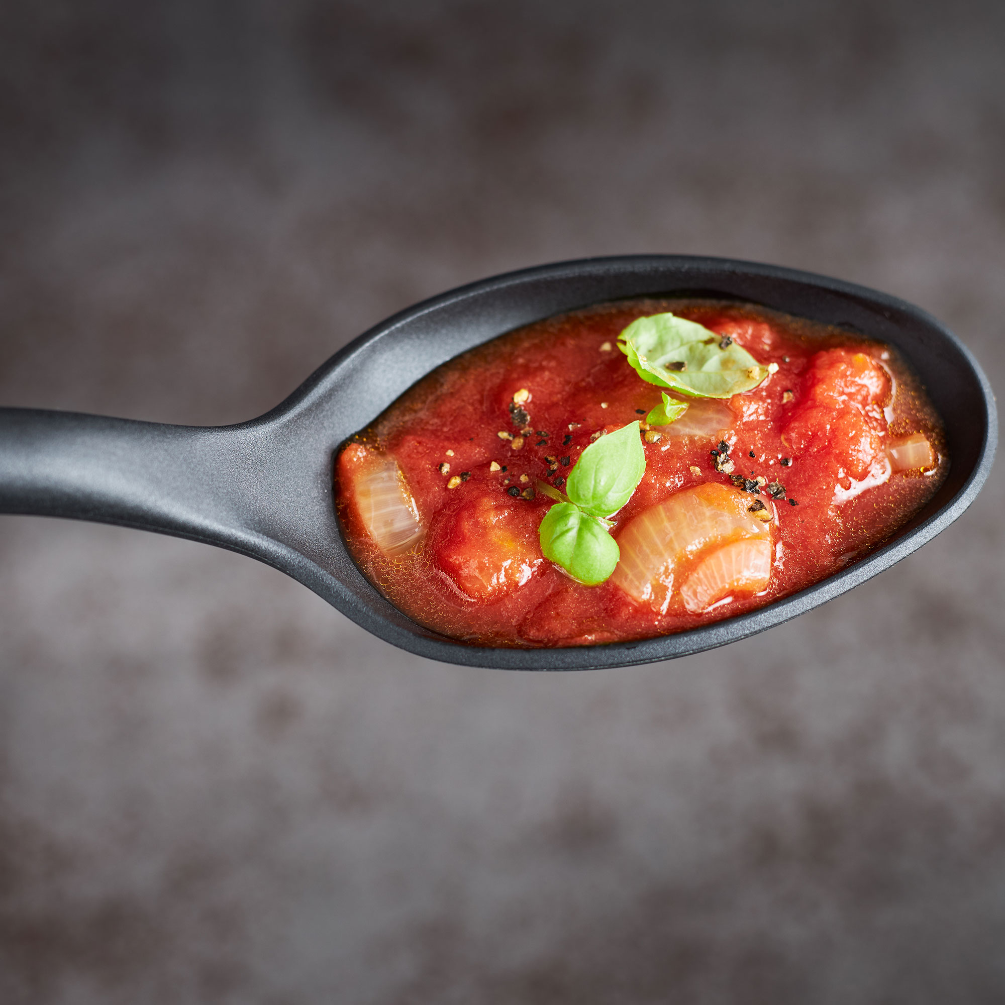 Gourmet-Set mit Tomatensoße in einem schwarzen Löffel, garniert mit Basilikum.