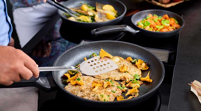 Meat and chanterelles in a pan are turned with stainless steel turner.