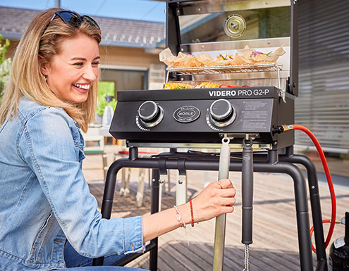 Woman hangs grill tongs on hook bar on mobile gas grill