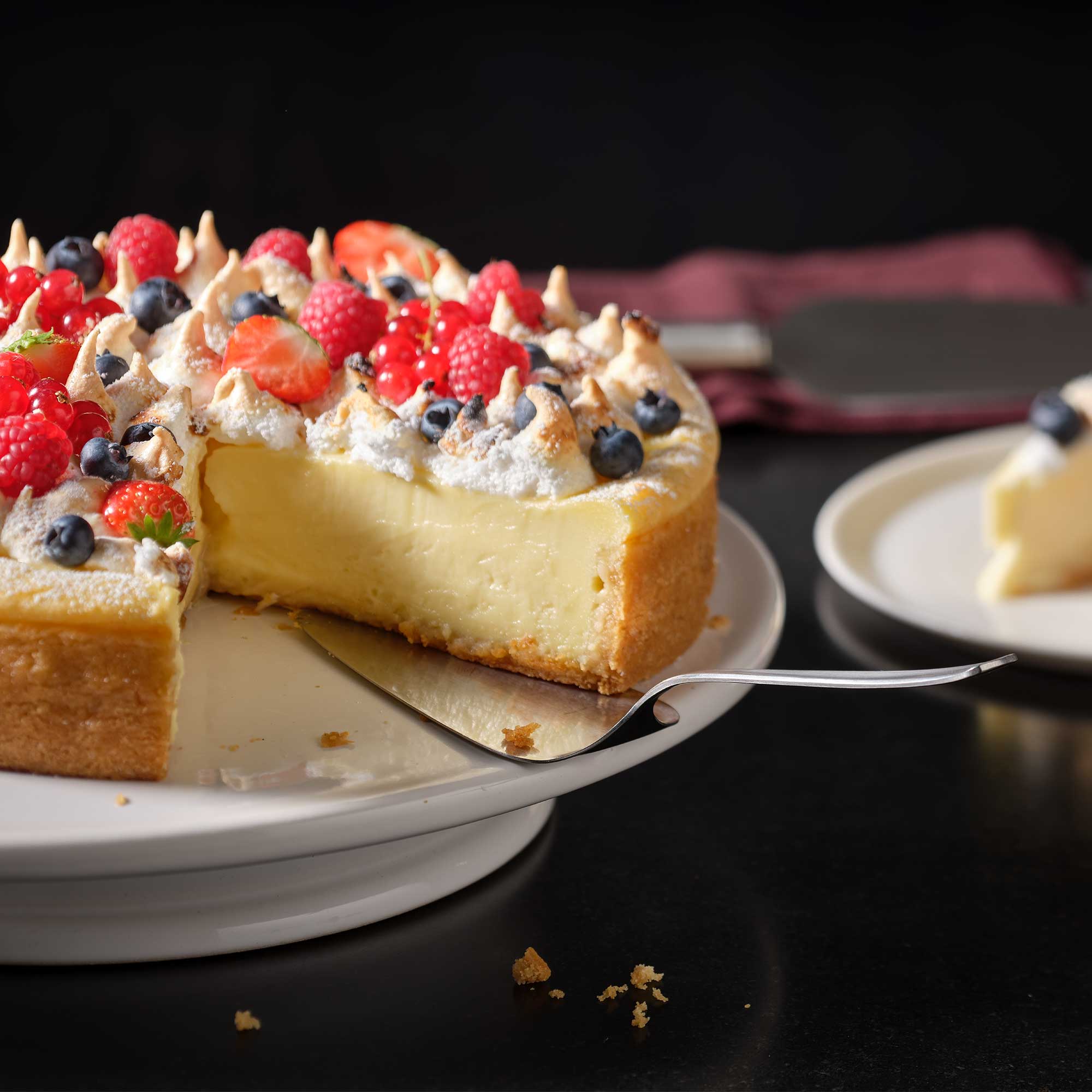 RÖSLE Tortenschaufel mit Käsekuchen Tortenschaufel aus Edelstahl hebt ein Stück Käsekuchen mit Beeren und Baiser von einer Torte...