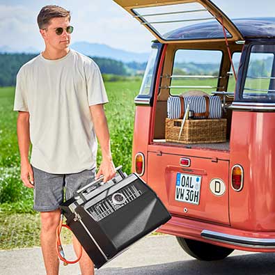 RÖSLE Gasgrill BBQ-Portable Videro G2-P Mann trägt Videro G2-P mit einer Hand am Deckelgriff aus dem VW Bully.