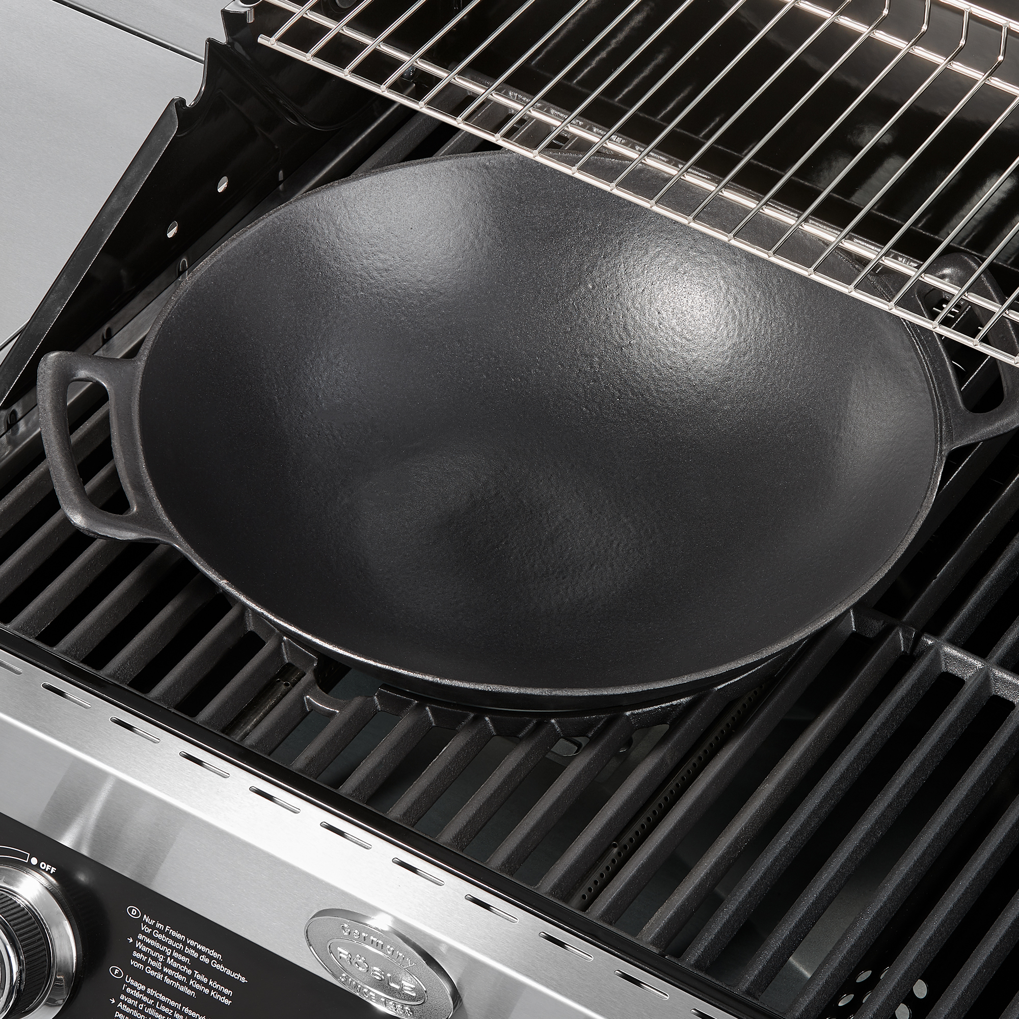 RÖSLE Wok Vario, 36 cm Wok Vario, 36 cm, aus Gusseisen, auf einem Grillrost platziert.