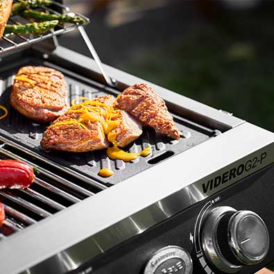 RÖSLE Gasgrill BBQ-Portable Videro G2-P Grillplatte mit Fleisch auf dem Videro G2-P.